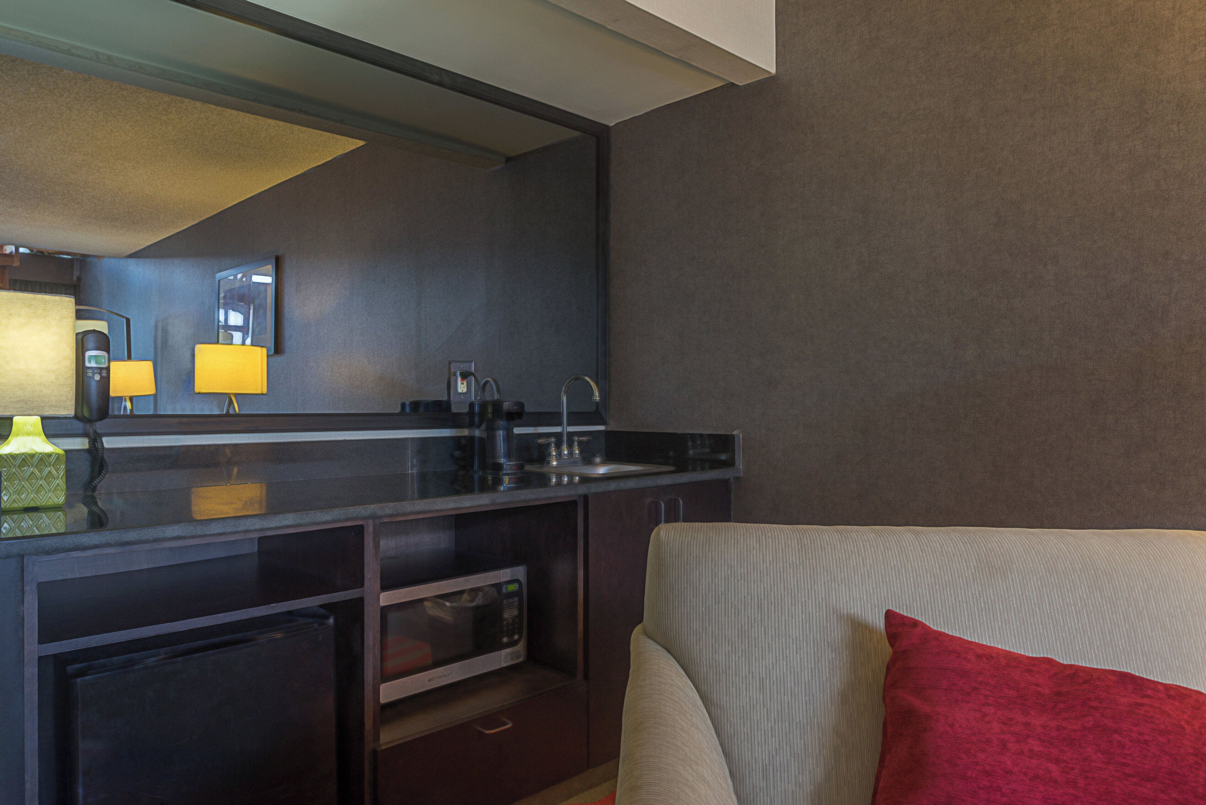 A hotel room with a kitchenette, a bed, and a red pillow.