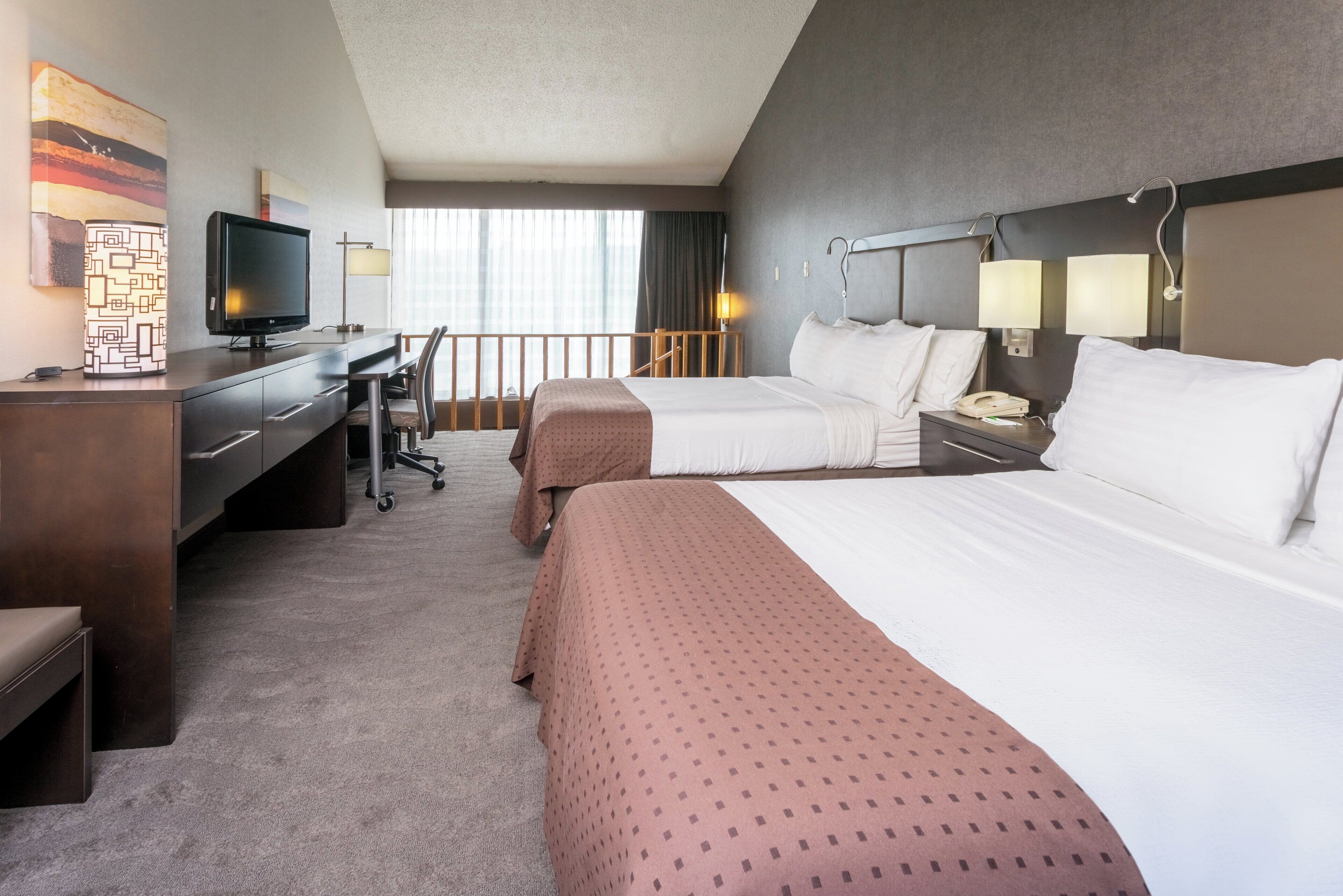 Habitación de hotel con dos camas, un escritorio con computadora, televisor y balcón con vista.
