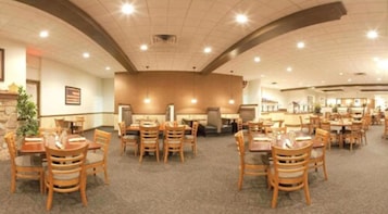 A spacious dining area with multiple tables and chairs, a stone accent wall, and a large American flag.