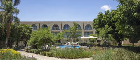 A hotel with a swimming pool, outdoor seating, and lush landscaping.