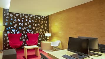 Um espaço de escritório moderno com duas cadeiras vermelhas, uma mesa redonda, uma escrivaninha com dois monitores e uma luminária.