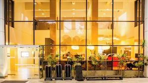 Entrada de hotel con fachada de vidrio, un mostrador de recepción y un carrito de equipaje.