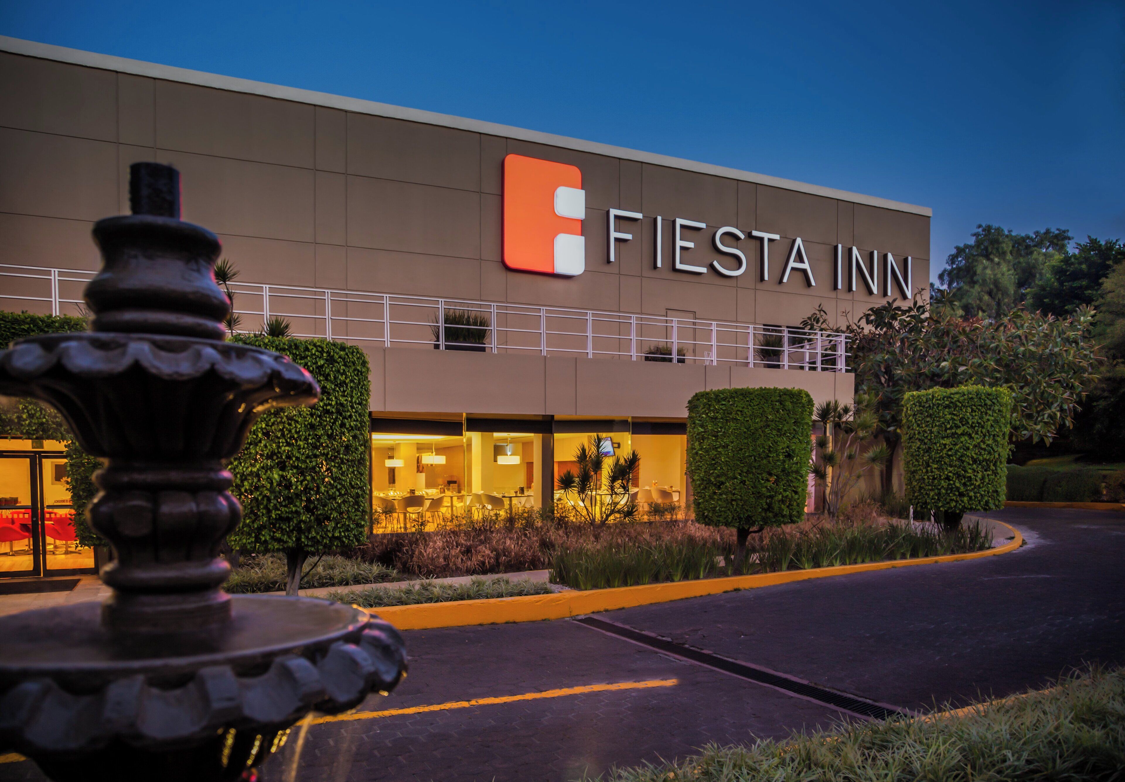 A Fiesta Inn hotel with a well-lit entrance and a fountain in the foreground.