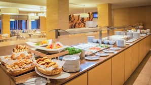 Un bufé con diversos alimentos, como panes, ensaladas y perros calientes, en un espacio amplio y luminoso con decoración moderna.