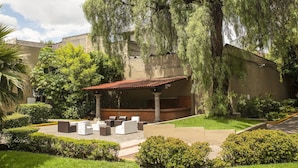 Un patio con mobiliario exterior, un árbol grande y un edificio de techo rojo.