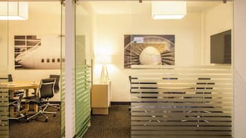 Un espacio de oficina moderno con un separador de vidrio, una mesa de conferencias, sillas de oficina, una lámpara y un elemento decorativo en la pared.