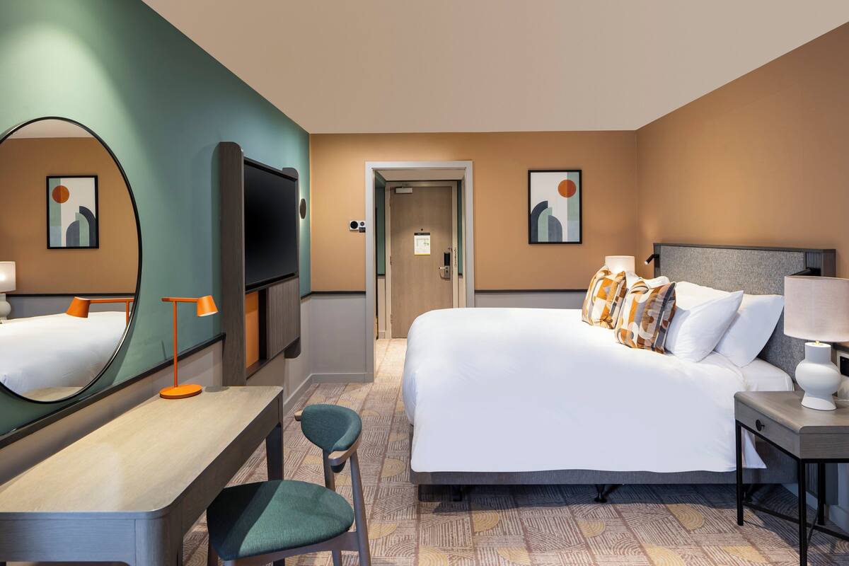 A hotel room with a bed, a desk, a chair, a TV, and a mirror.