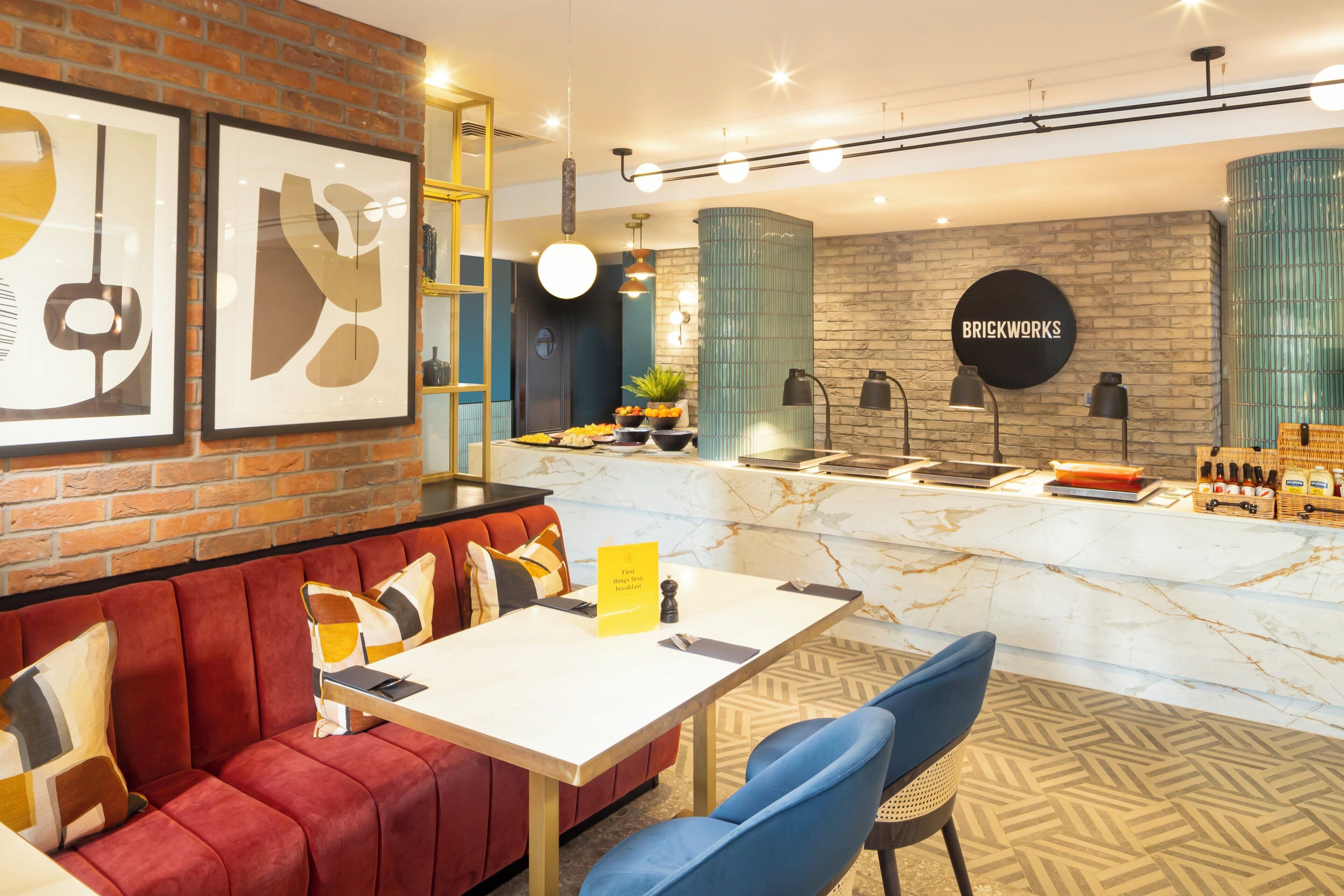 Un intérieur moderne avec un mur de briques, un canapé rouge, un comptoir en marbre et une enseigne portant l’inscription « BRICKWORKS ».