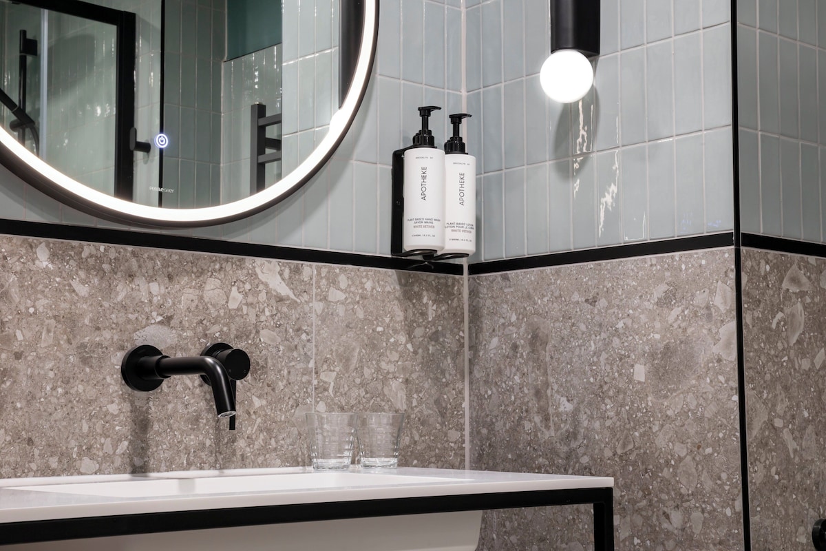 A bathroom with a sink, two bottles of Artheme, a mirror, and a faucet.