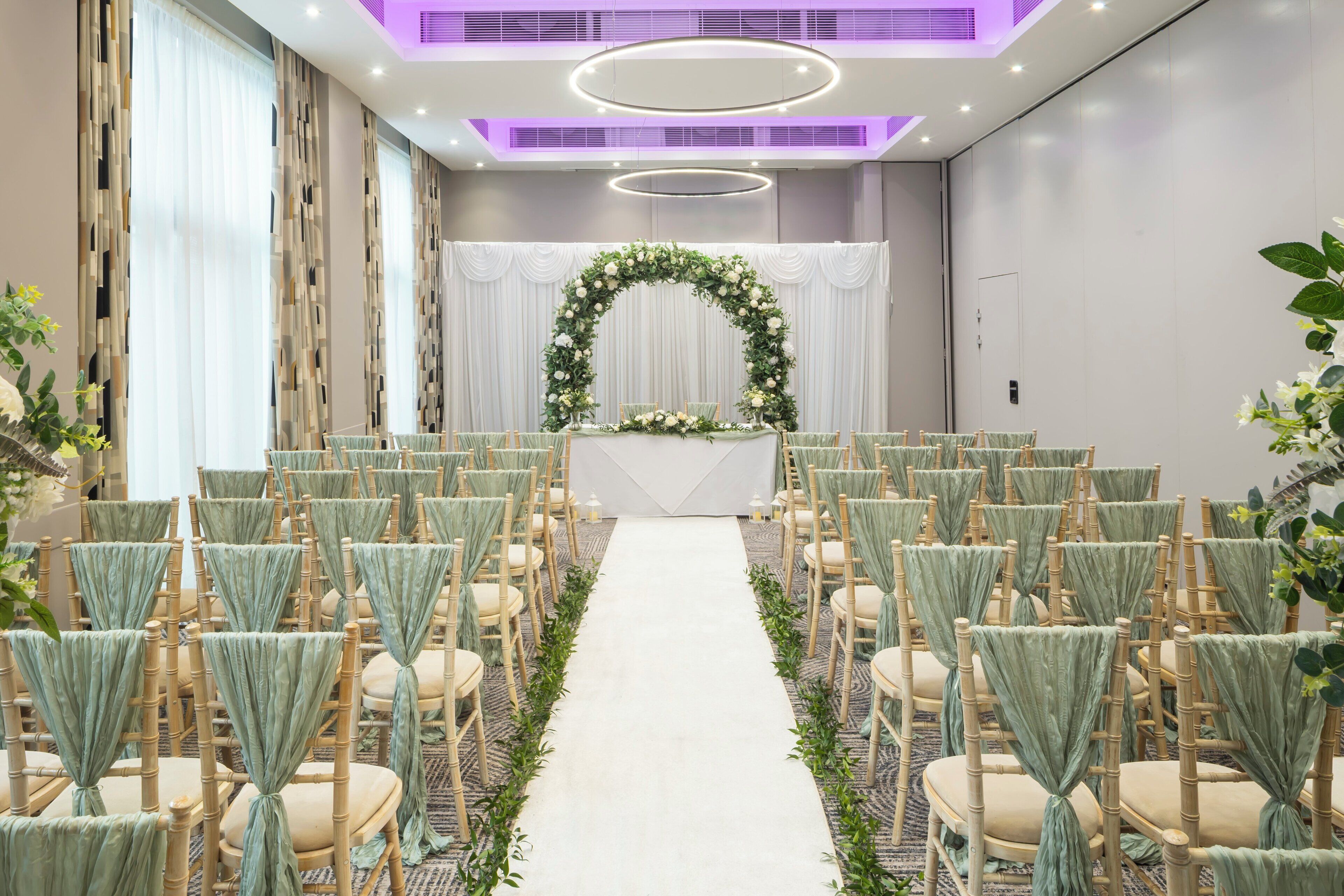 Decoración para una ceremonia de boda, con un arco floral, pasillo y filas de sillas.