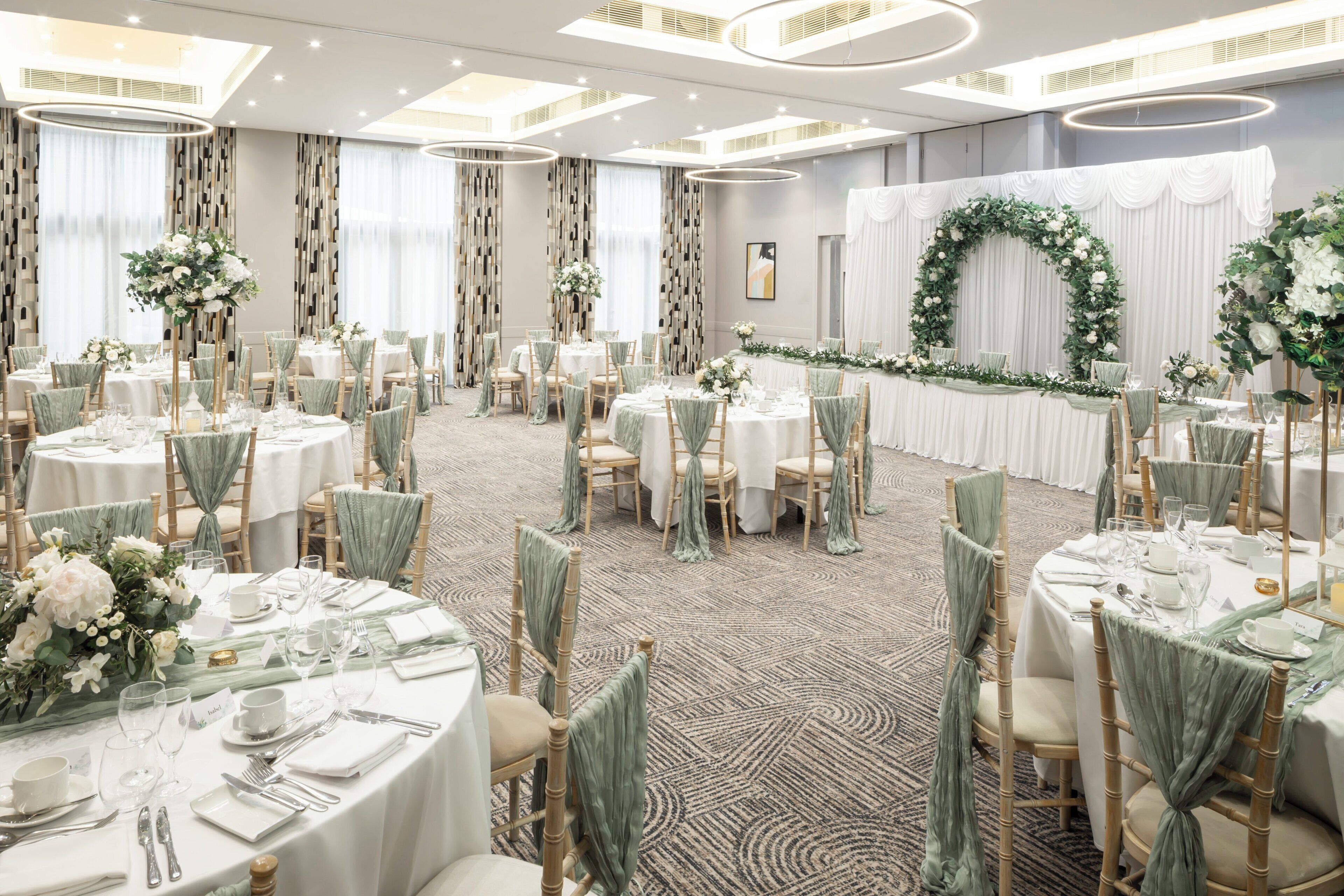 A banquet hall with round tables, green chair covers, and floral centerpieces.