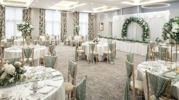 A banquet hall with round tables, green chair covers, and floral centerpieces.