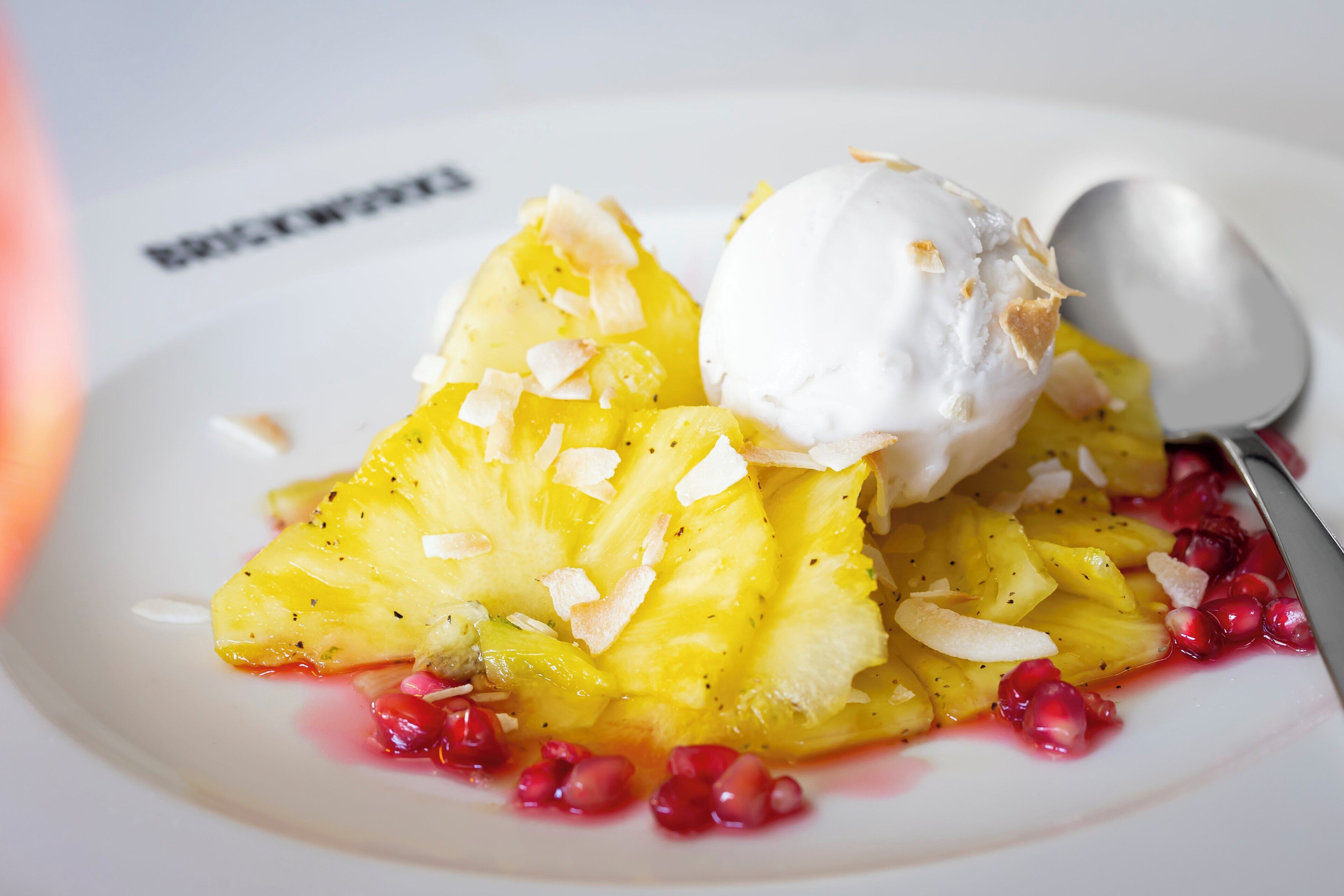 Un postre con piña, coco y granada sobre un plato blanco.