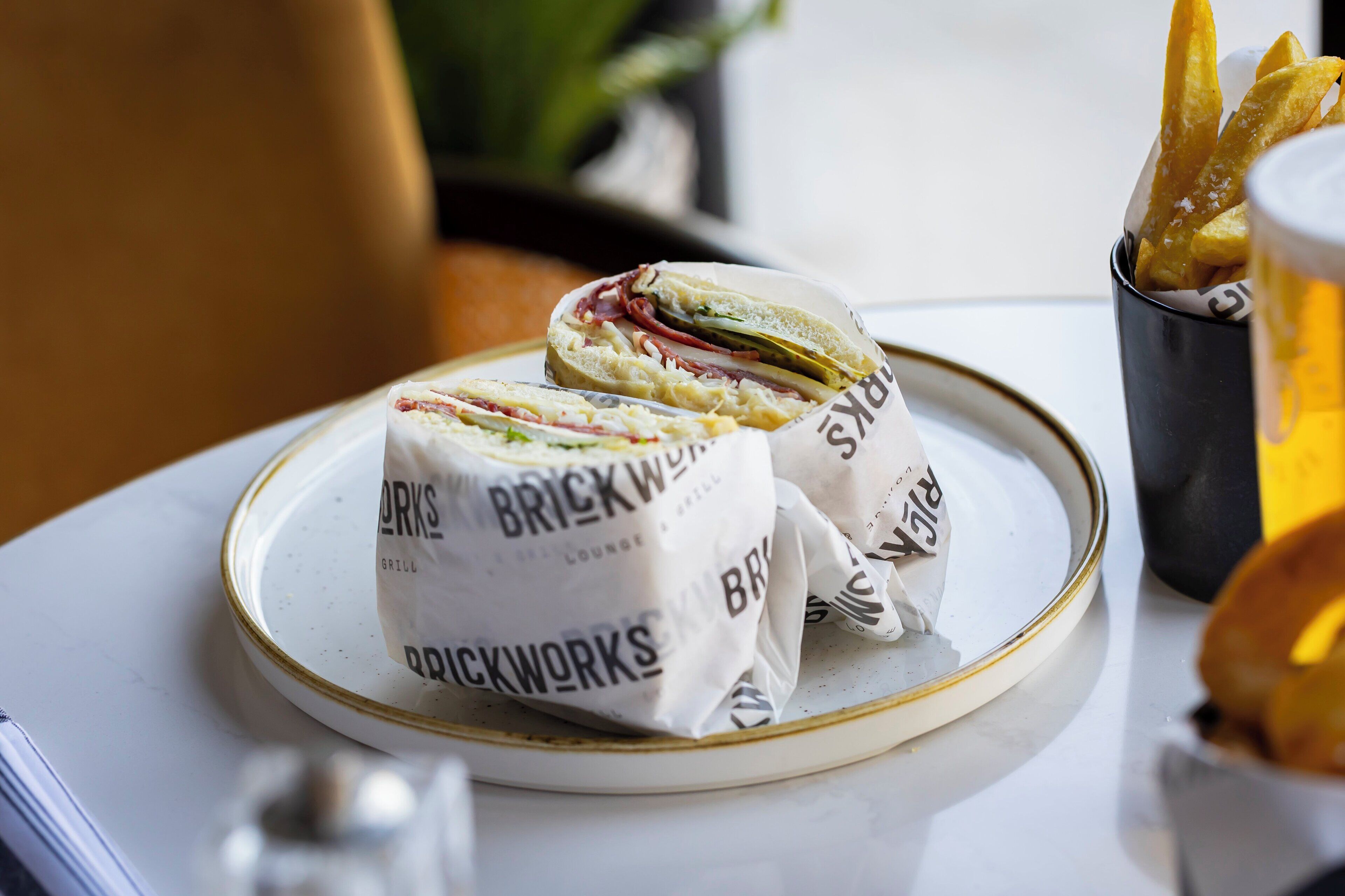 A plate with two sandwiches and a cup of beer on a table.