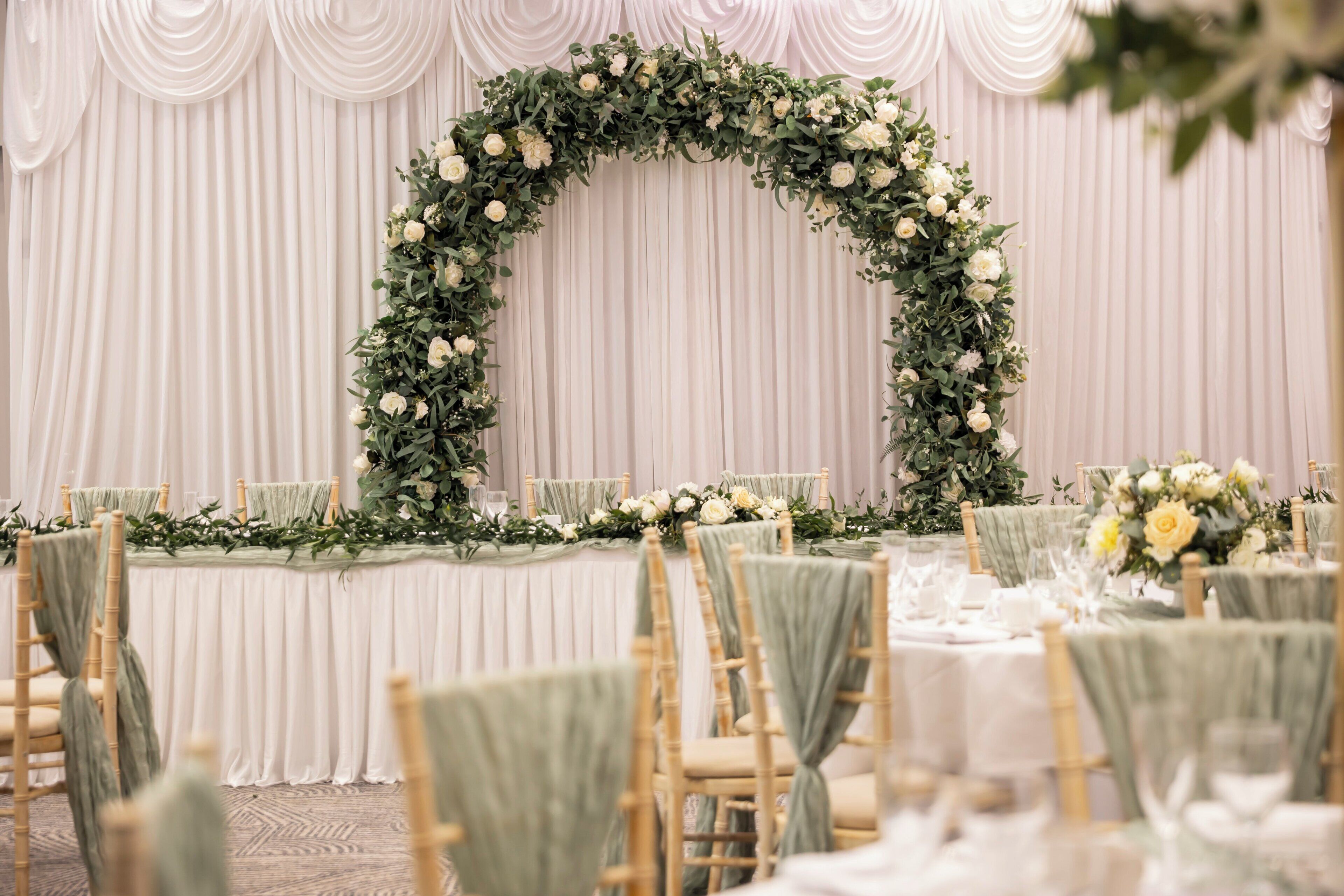 A banquet hall with tiered seating, white drapery, and floral centerpieces.