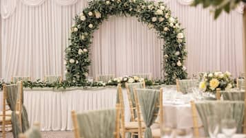 A banquet hall with tiered seating, white drapery, and floral centerpieces.