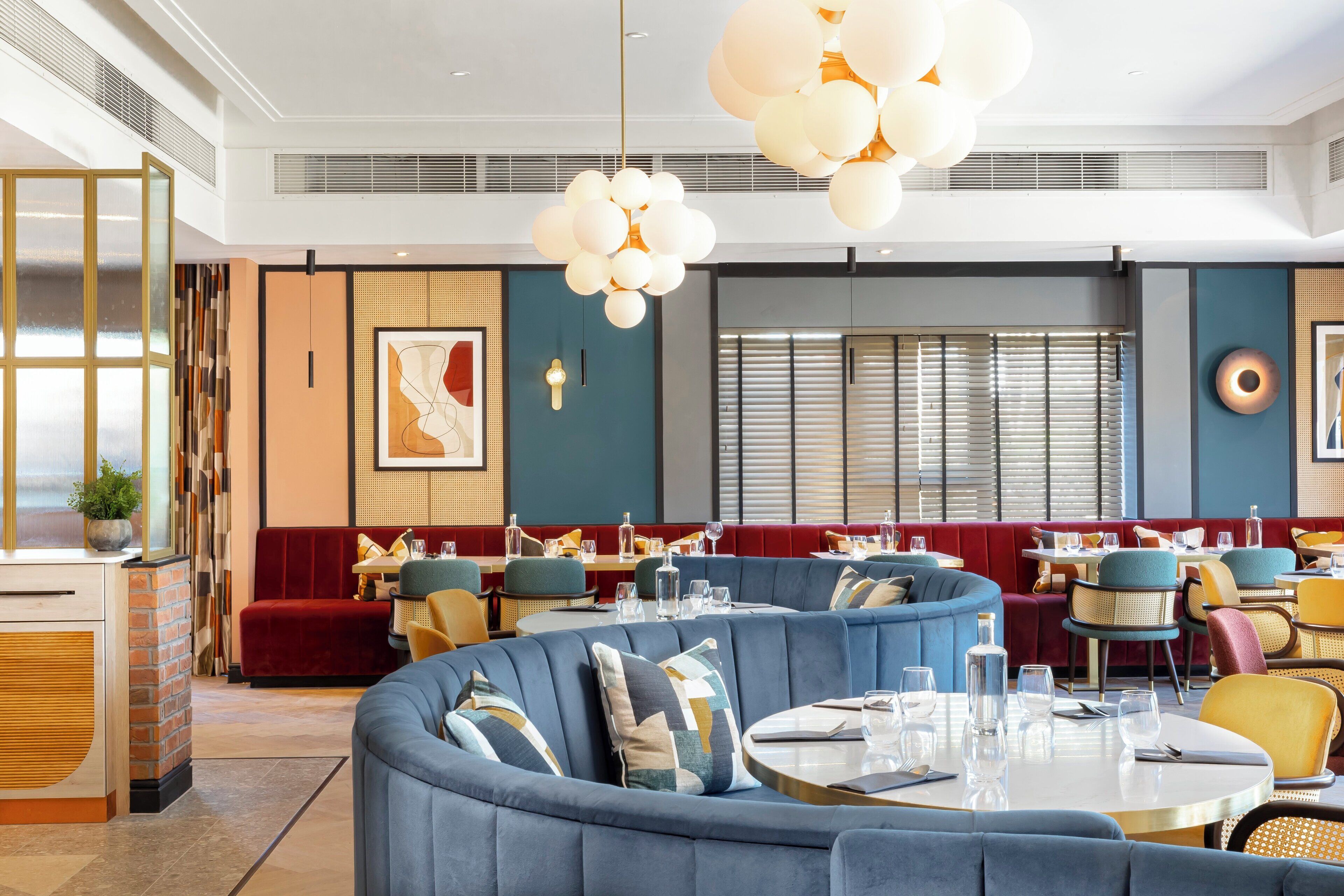 A modern restaurant interior with round tables, blue cushioned seating, and decorative lighting.