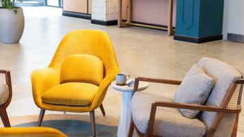 A modern lobby with a yellow armchair and a wooden chair with a cushion.