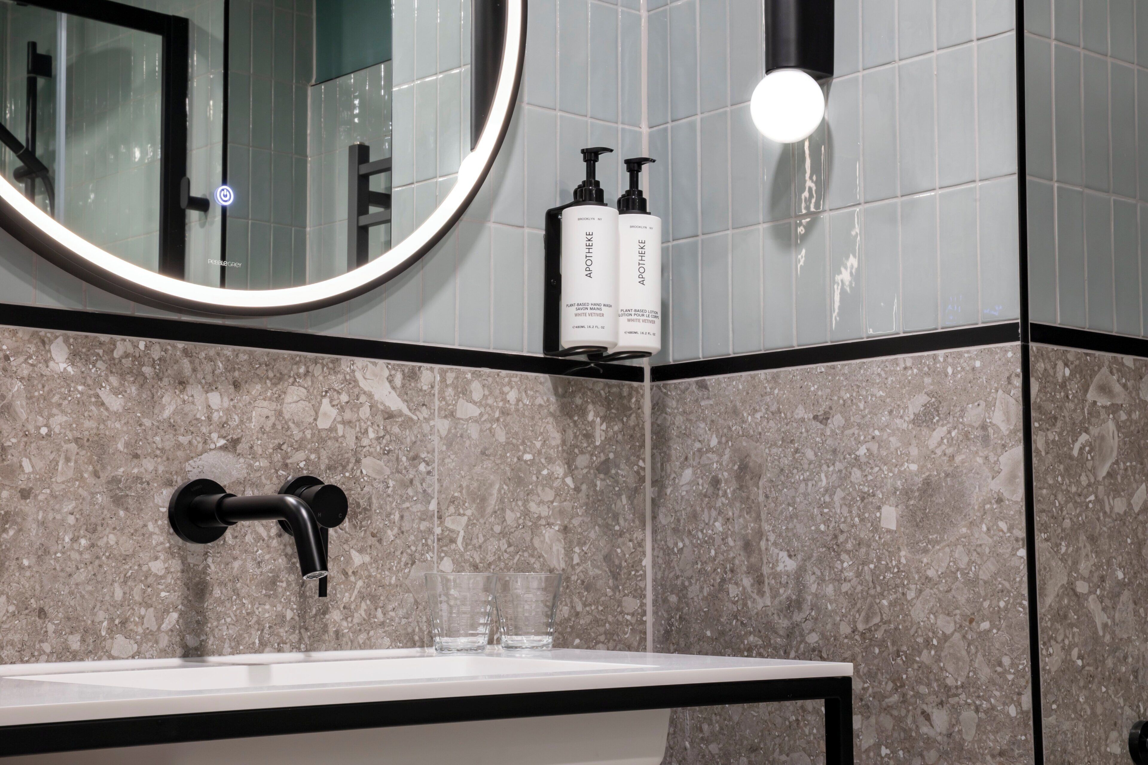 Un baño con un lavamanos, dos botellas de Artheme, un espejo y un grifo.