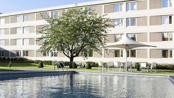 A modern hotel with a swimming pool, outdoor seating, and a large tree in the center.