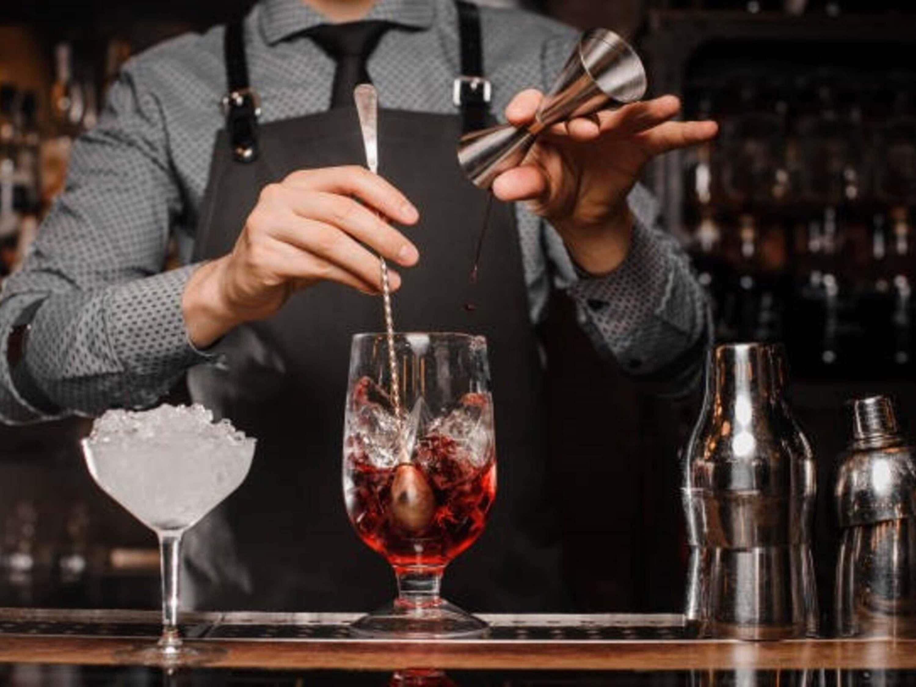 Un barman prépare un cocktail à l’aide d’un shaker et d’un verre contenant un liquide rouge.