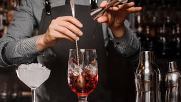 Un barman prépare un cocktail à l’aide d’un shaker et d’un verre contenant un liquide rouge.