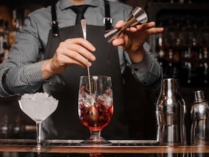 A bartender preparing a cocktail with a shaker and a glass of red liquid. - Novotel Antwerpen (Antwerp)