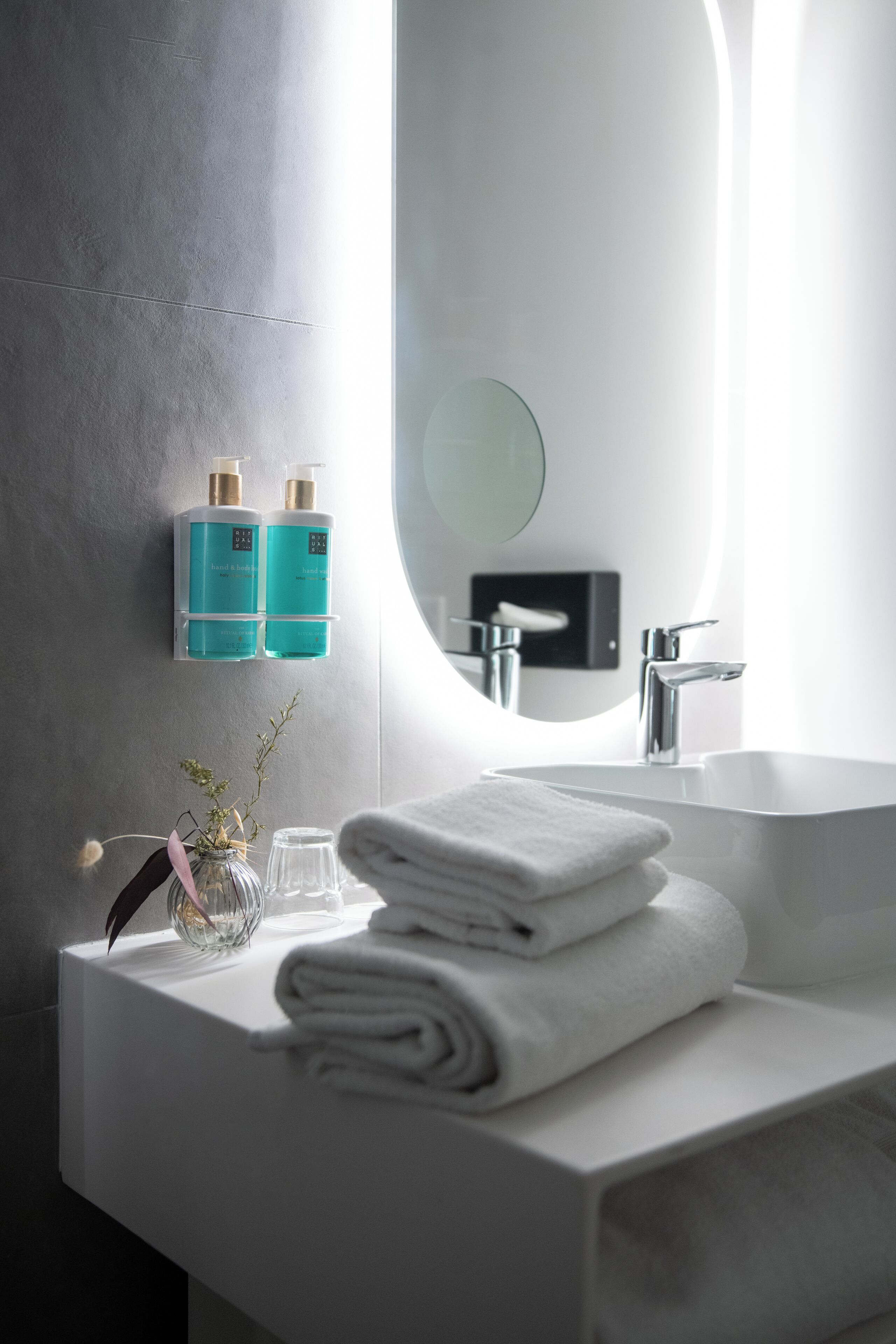 Un baño moderno con un lavabo blanco, un espejo grande y dos botellas color turquesa sobre una repisa de pared.