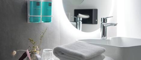 Un baño moderno con un lavabo blanco, un espejo grande y dos botellas color turquesa sobre una repisa de pared.