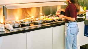 Una mujer cocina en la encimera de una cocina comercial, con diversos utensilios y alimentos.