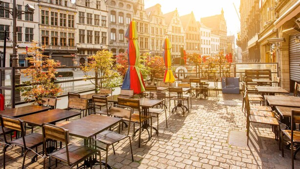 Un café al aire libre con mesas y sillas, rodeado de edificios históricos con arquitectura decorada.