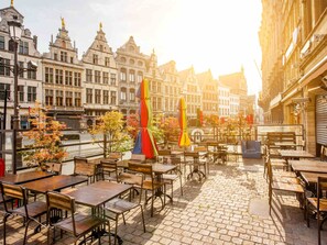 Un café al aire libre con mesas y sillas, rodeado de edificios históricos con arquitectura decorada.