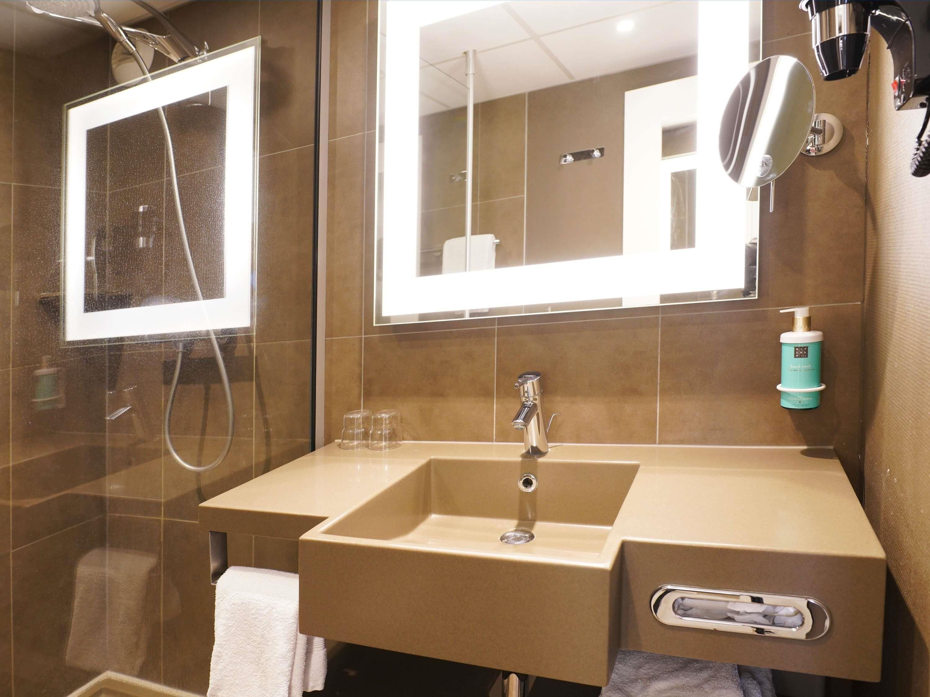 A bathroom with a glass-enclosed shower, a sink with a mirror above it, and a towel rack.