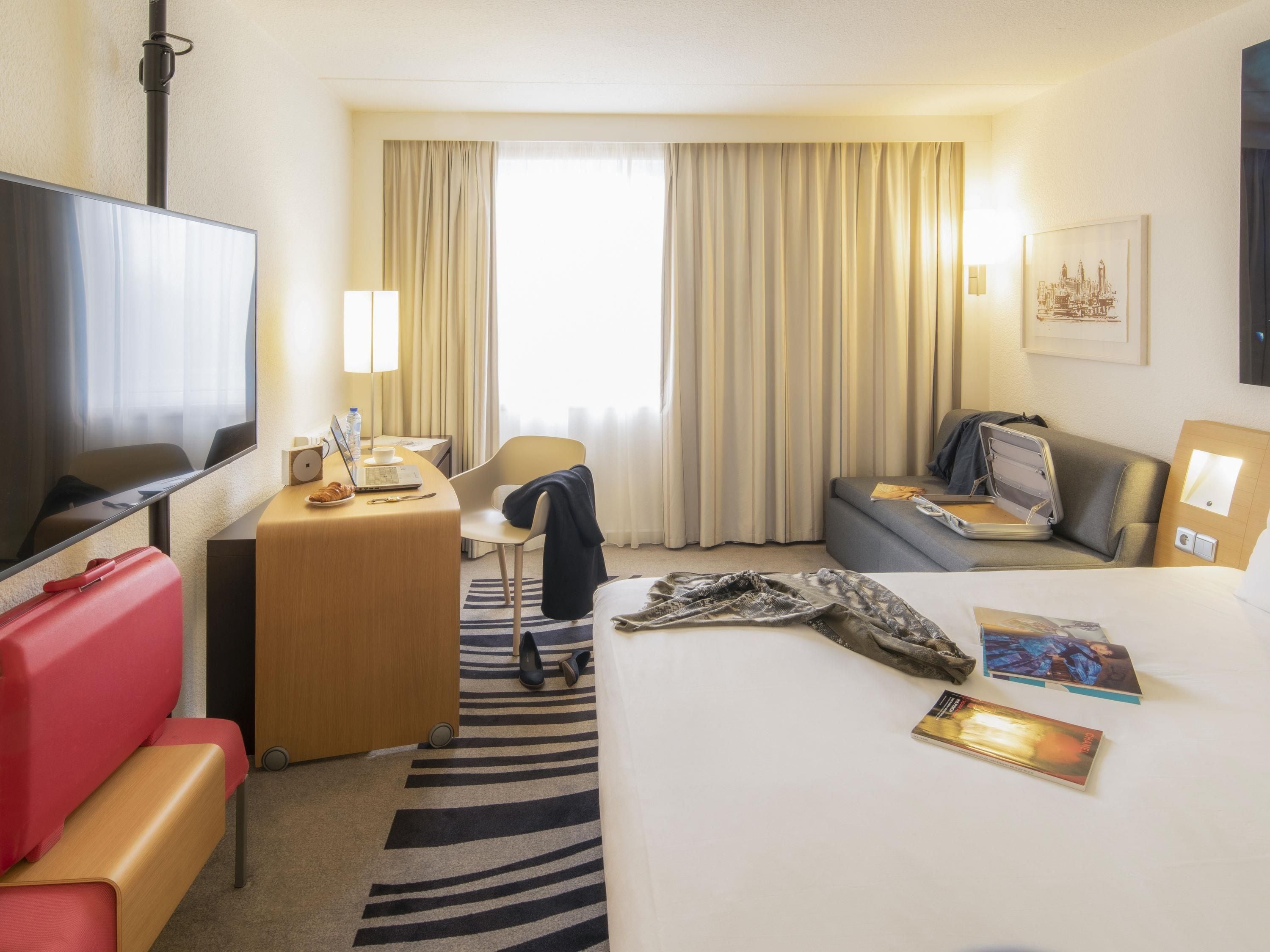 Habitación de hotel con cama, escritorio, silla, sofá, televisión y ventana con cortinas.