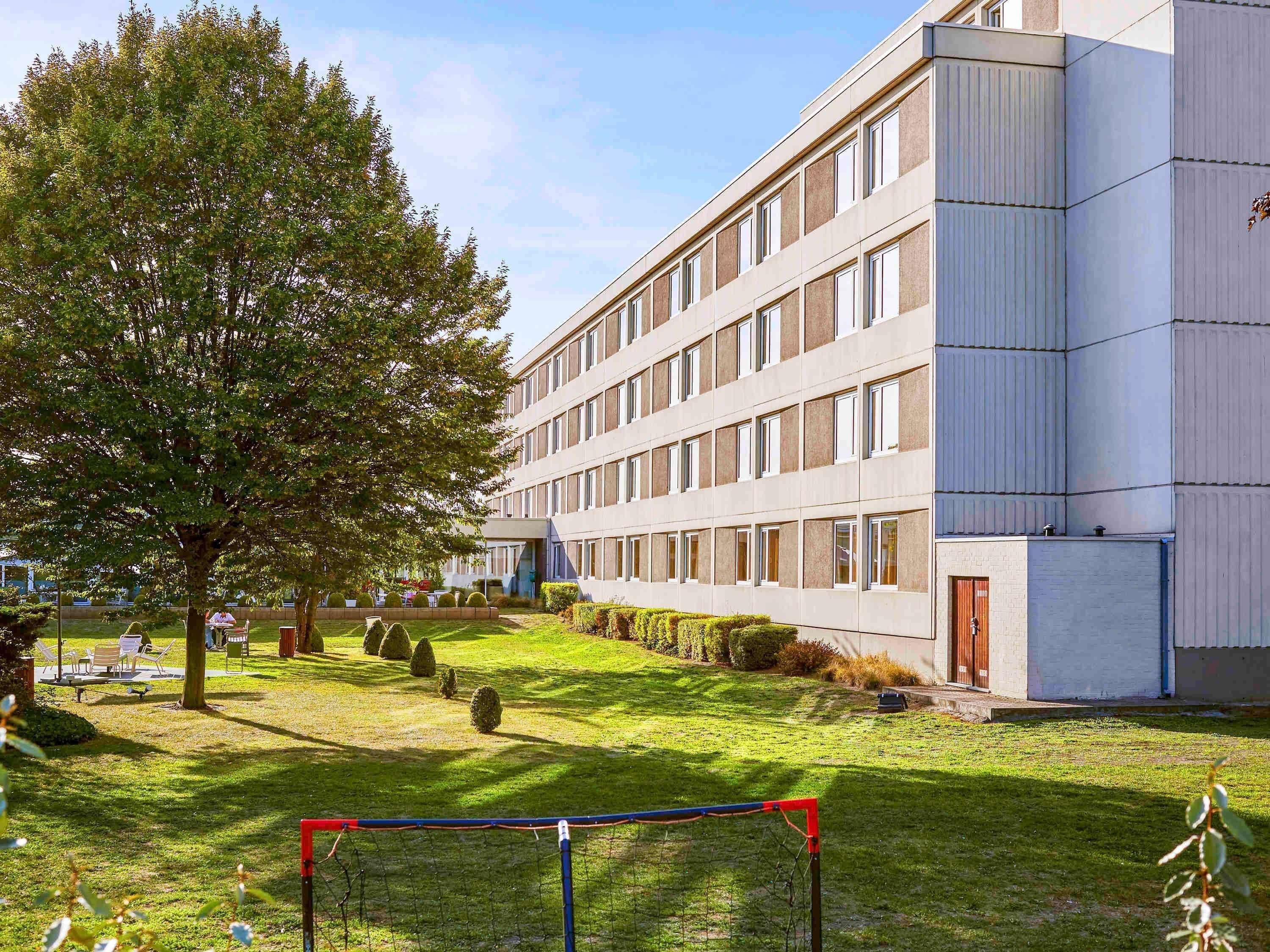 A modern building with a flat roof, large windows, and a well-maintained lawn with a soccer goal.