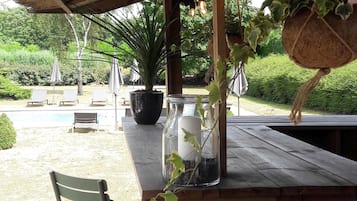 Un'area salotto esterna coperta con piscina, poltrona relax e piante in vaso.