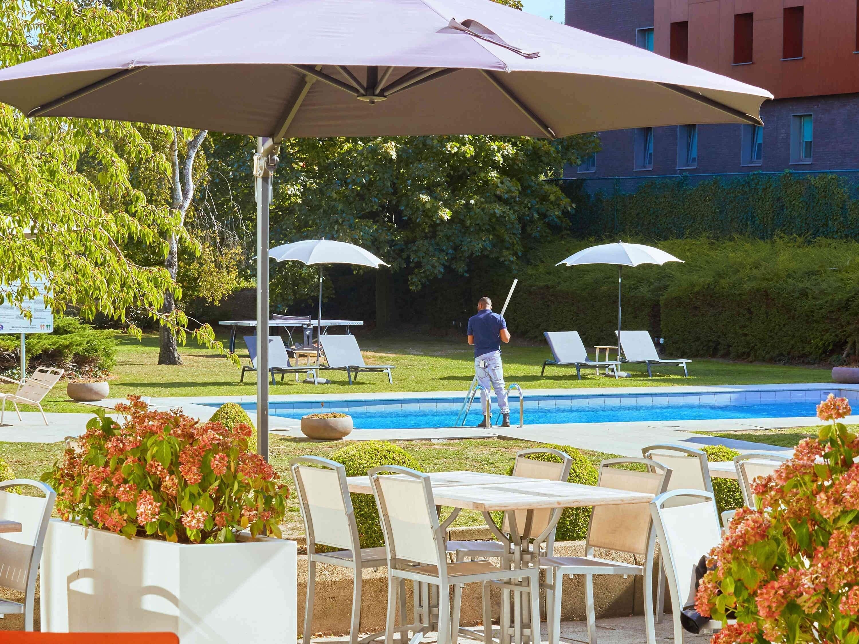 Uma área à beira da piscina com espreguiçadeiras, mesa e guarda-sóis.