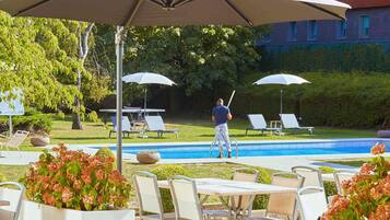 Uma área à beira da piscina com espreguiçadeiras, mesa e guarda-sóis.