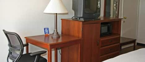 Een hotelkamer met een houten bureau, een televisie, een lamp, een stoel en een bed.