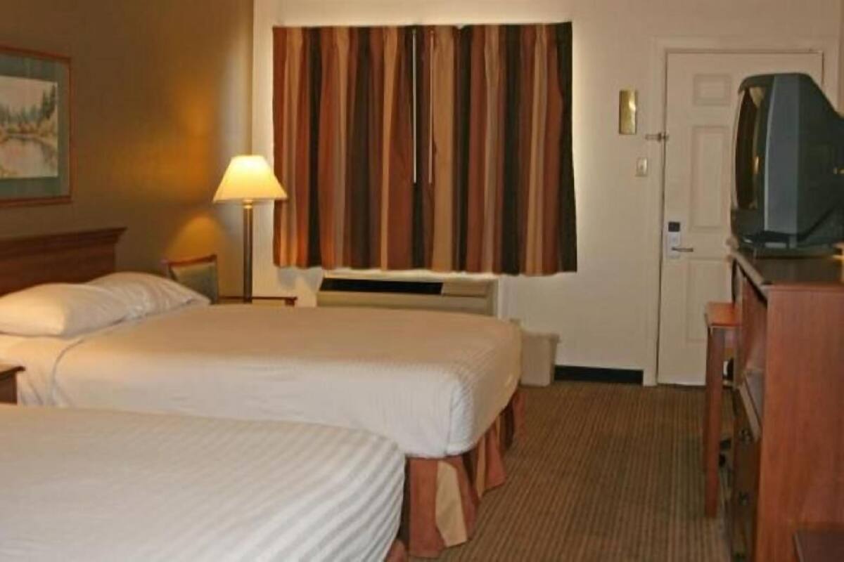 A hotel room with two beds, a television, a lamp, and a painting on the wall.
