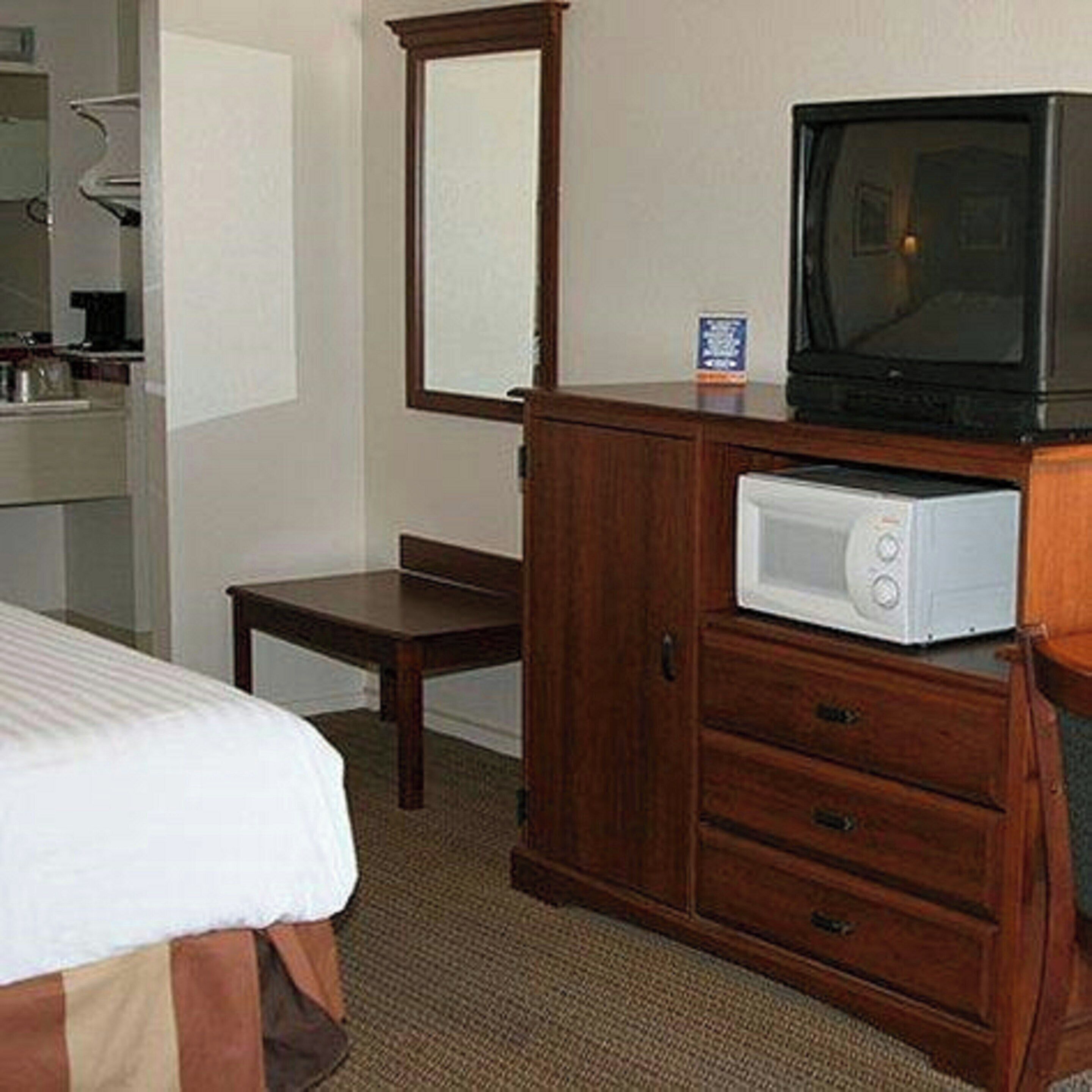 A hotel room with a bed, a wooden dresser, a microwave, and a television.