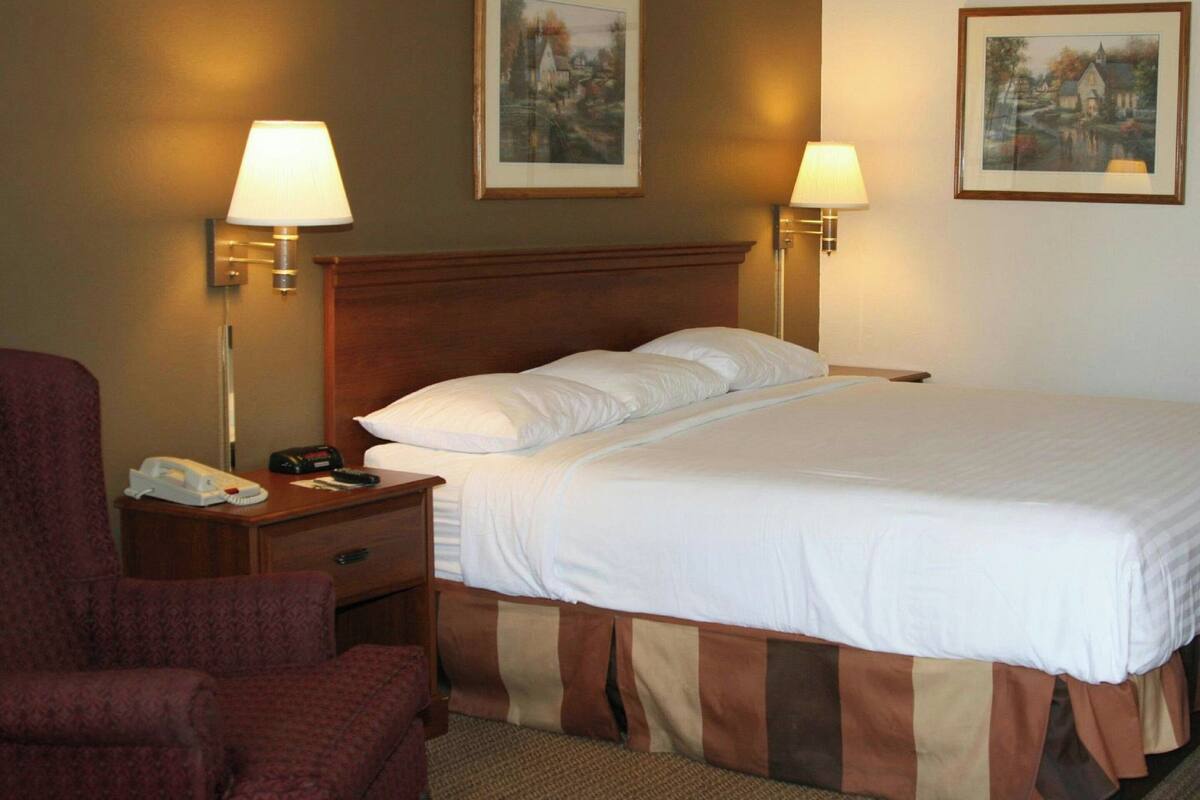 A hotel room with a large bed, two bedside lamps, a nightstand with a telephone and remote control, and two framed pictures on the wall.