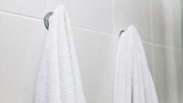 Un baño con paredes de azulejos blancos y dos toallas blancas colgadas en un perchero metálico.