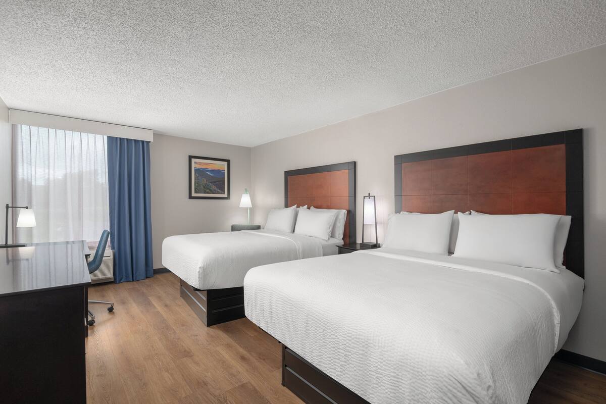 Ein Hotelzimmer mit zwei Betten, einem Schreibtisch und einem Fenster mit Vorhängen.