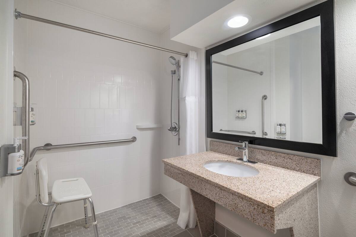 A bathroom with a white tiled shower area, a white toilet, a sink with a granite countertop, and a large mirror.