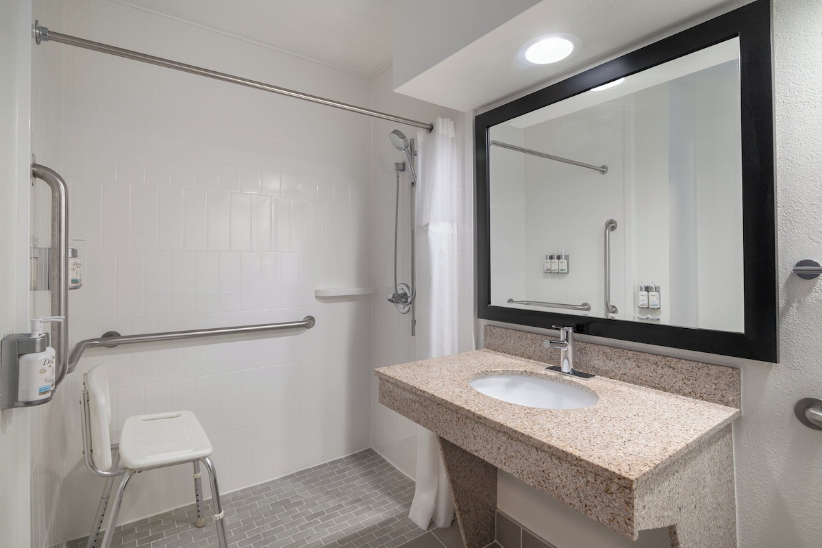 A bathroom with a white tiled shower area, a white toilet, a sink with a granite countertop, and a large mirror.