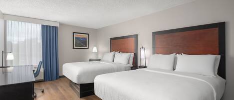 A hotel room with two beds, a desk, and a window with curtains.