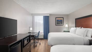 Habitación de hotel con televisor de pantalla plana, un escritorio con silla, dos camas, una ventana con cortinas y un cuadro en la pared.