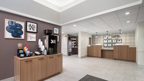 A modern reception area with a wooden reception desk, framed artwork on the walls, a coffee machine, and a vending machine. - Garner Hotel Wytheville East by IHG (Wytheville)