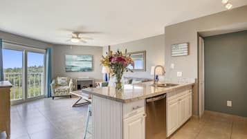 A modern kitchen with a central island, a dining area with a chair, and a view through large windows.